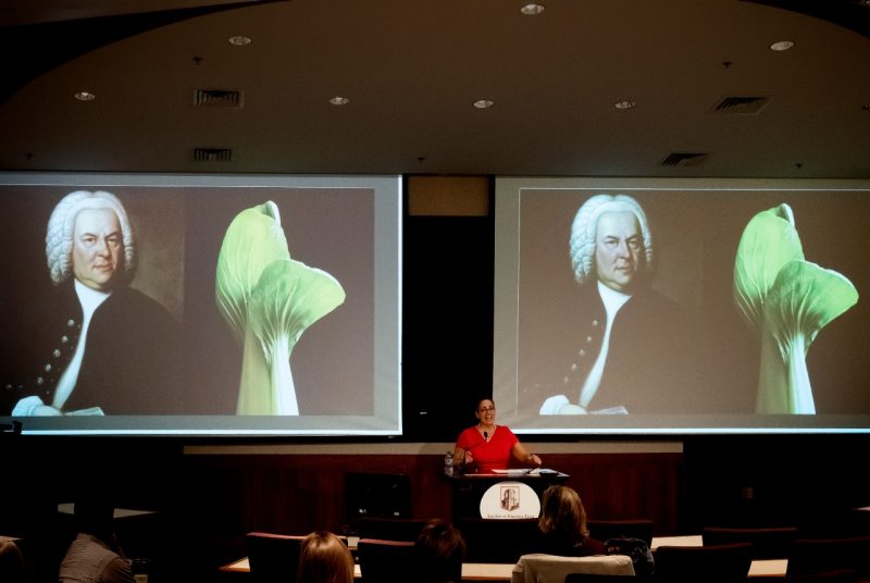 Laura Belmonte at the podium, with Bach and bok choy projected behind her