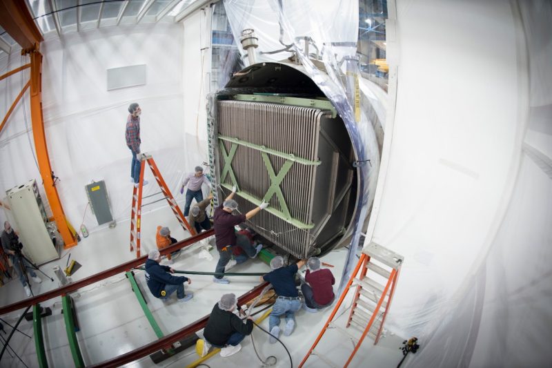 In this 2013 photo, workers install a component of MicroBooNE’s precision detector, called a time projection chamber, into the cylindrical container, or cryostat. Here a massive box-like structure is placed inside a large tube that will serve as the housing for the detector. Photo by Reidar Hahn, Fermilab.