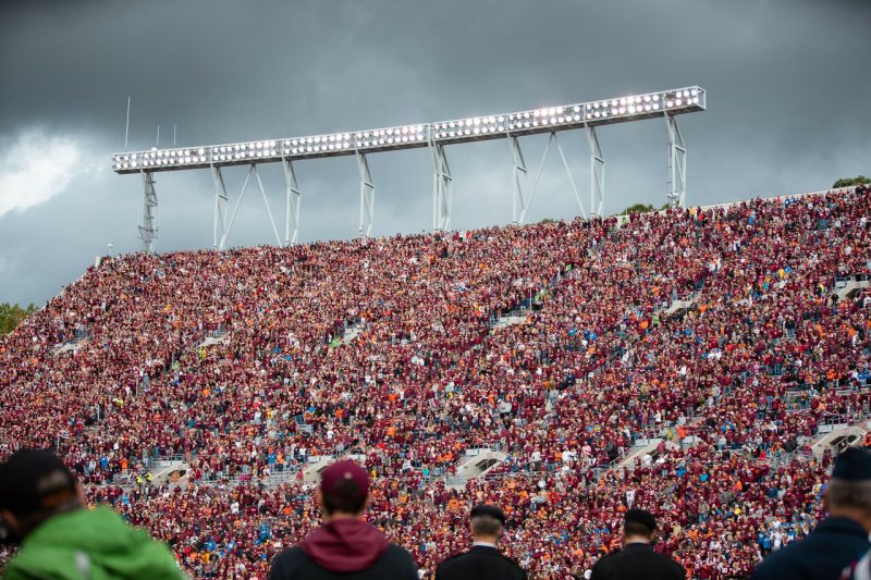 Image shows fans in the stands under a cloudy sky for an October football game. 