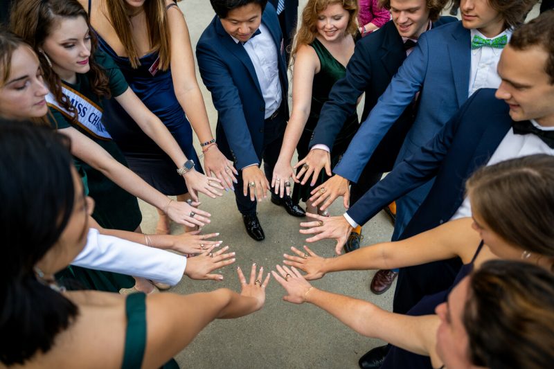 students in a circle with arms out wearing new class rings