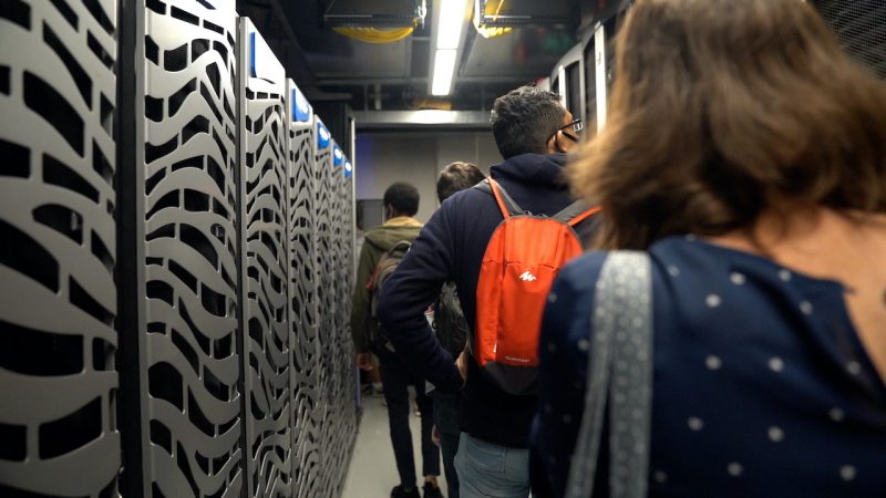  a line of students walk between rows of high-performance computing clusters.