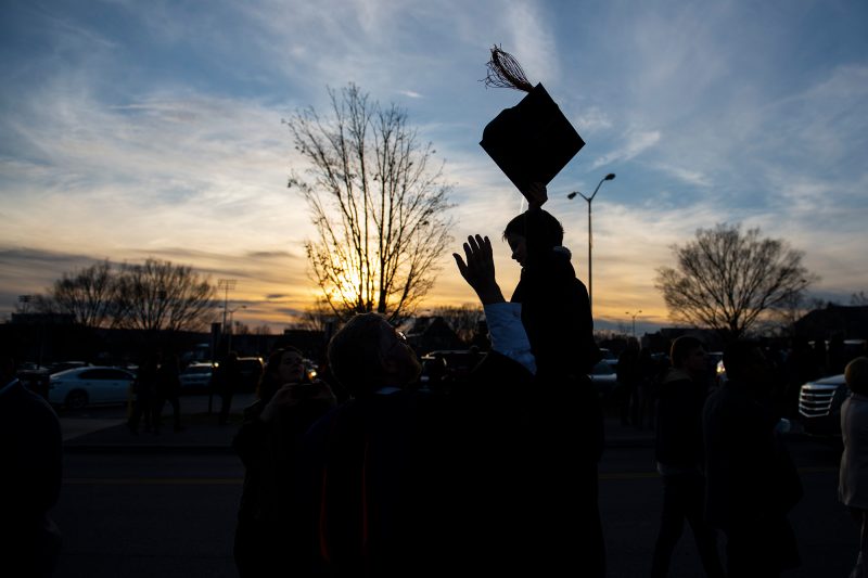 Image shows a young child held up in silhouette with graduate cap