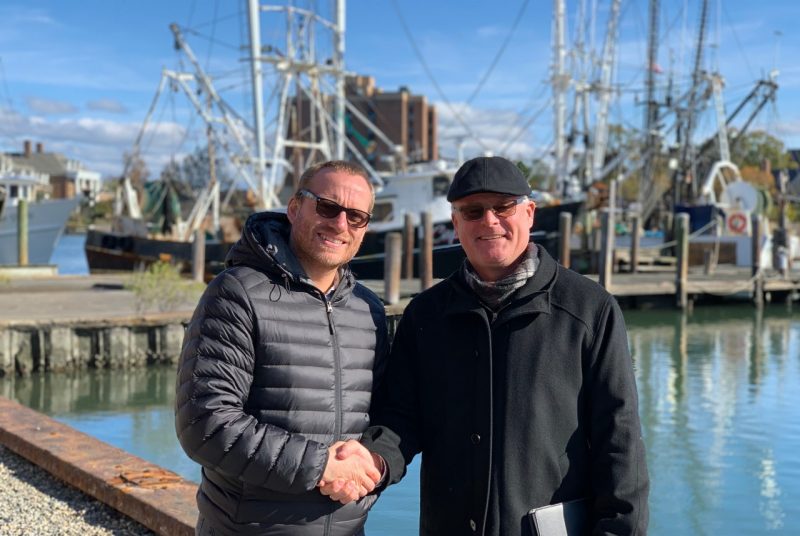 Robert Weiss, director of the Center for Coastal Studies, and Michael Schwarz, director of the Virginia Seafood AREC shake hands in front of a fishing boat on the Hampton River.