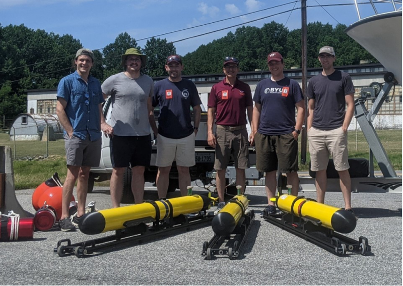 Dan Stilwell stands with team of graduate students behind autonomous underwater vehicles.