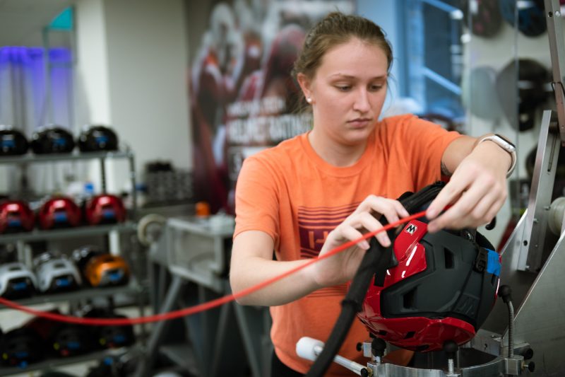 Female student sets up an impact test for a red snow sports helmet in a lab. 