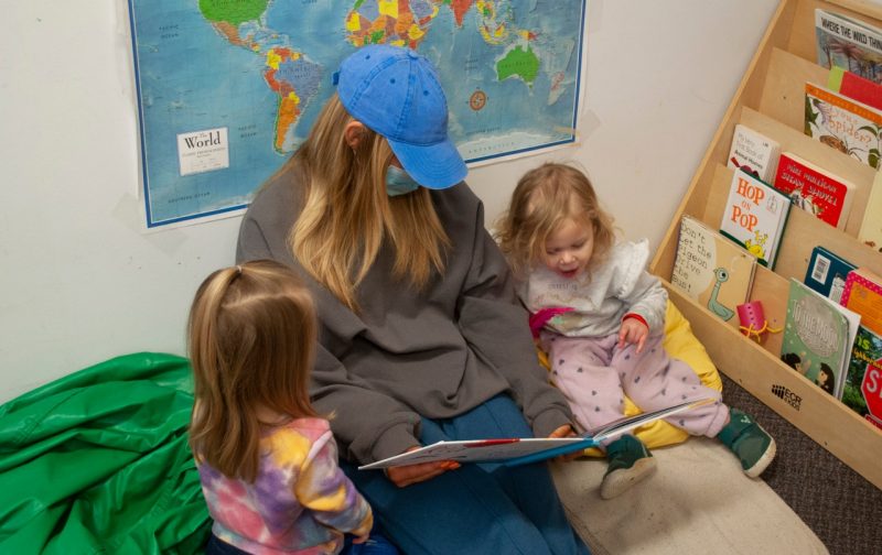 image of a blond woman in a ballcap reading to two little girls at Little Hokie Hangout