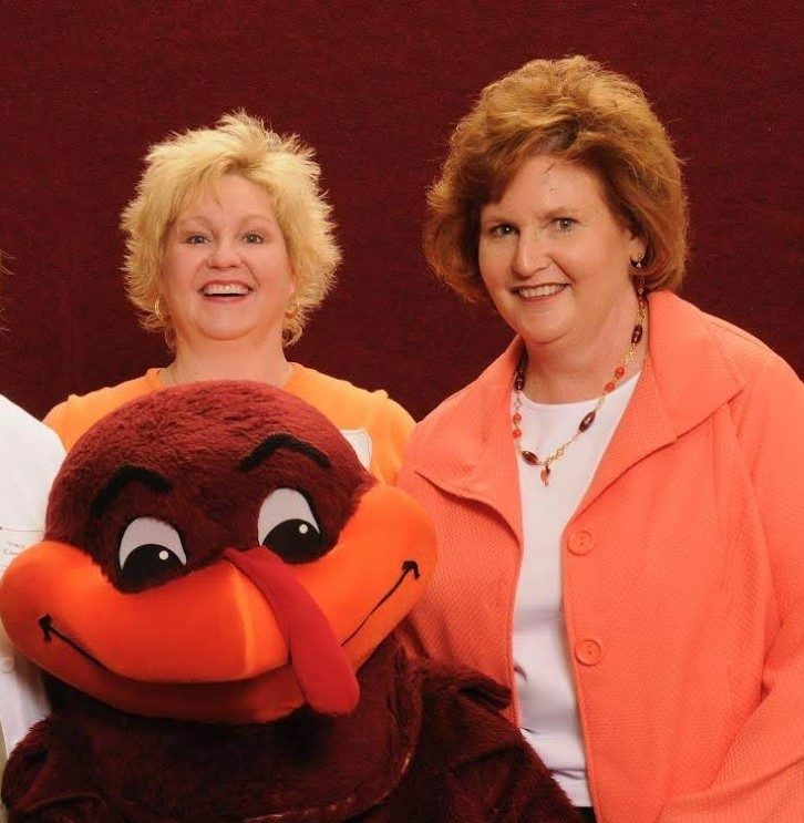 Susan Lucas is on the right, smiling beside her sister Nancy Lucas as they pose with the Hokie Bird.