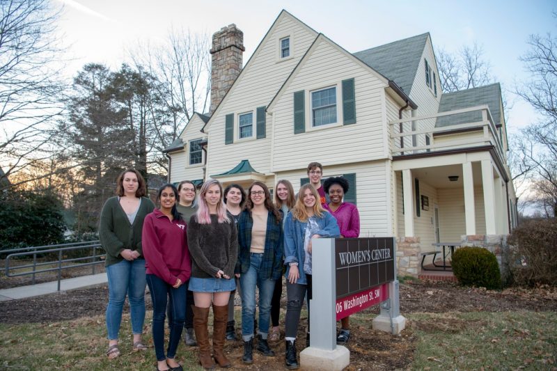 A group of students stands in front of the yellow house that is home to the Women's Center at Virginia Tech. 