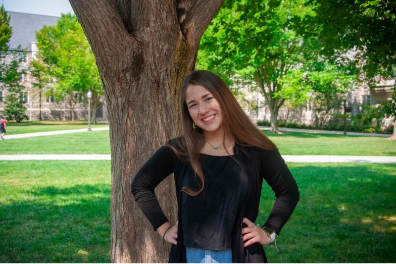 Betsabeth Oropeza A portrait of Betsabeth standing in front of a tree trunk.