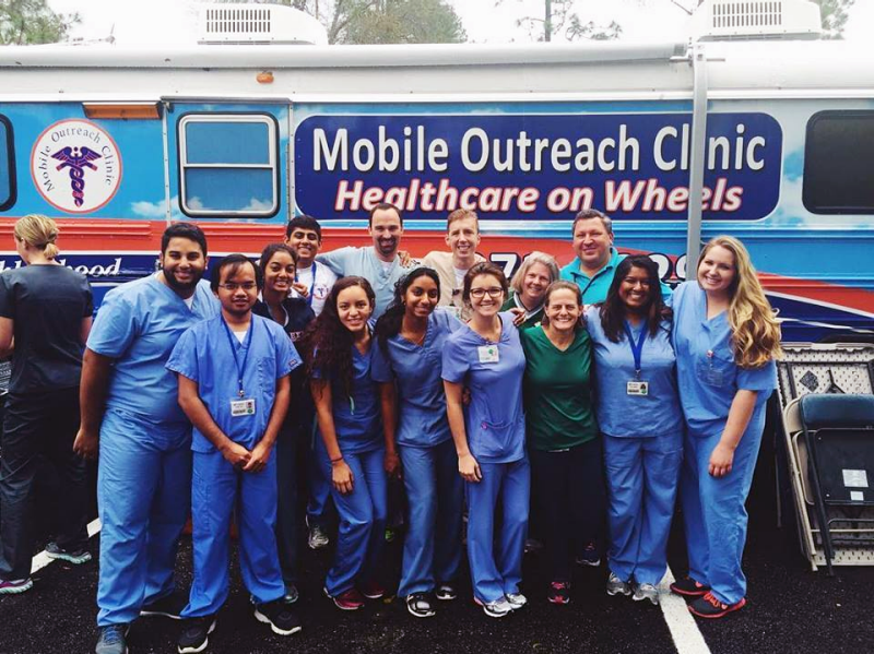 Image of a group of medical students and health professionals in front of a school bus that has been converted into a mobile health clinic.