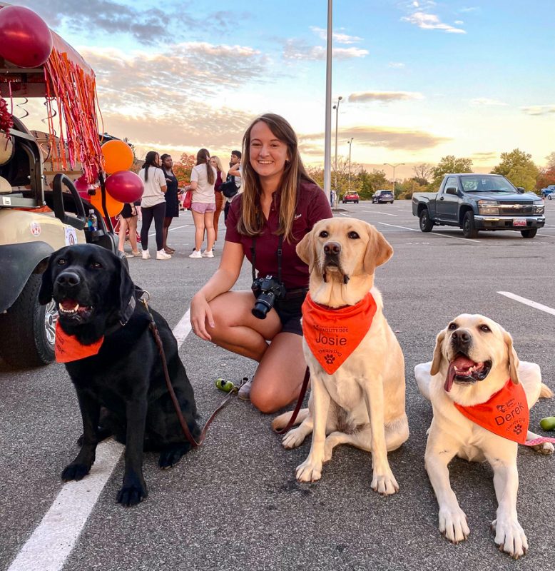 Kensley Bullins poses in a parking lot with three of the Cook Counseling Center therapy dogs, Wagner, Josie, and Derek.
