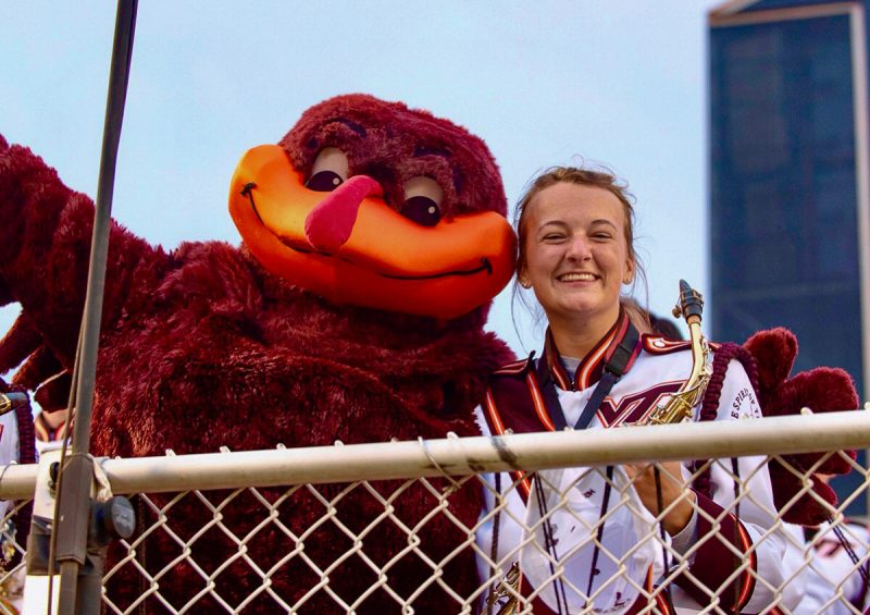 Hokie Bird and Kensley Bullins in her Marching Virginians uniform and holding saxophone pose together in Lane Stadium.