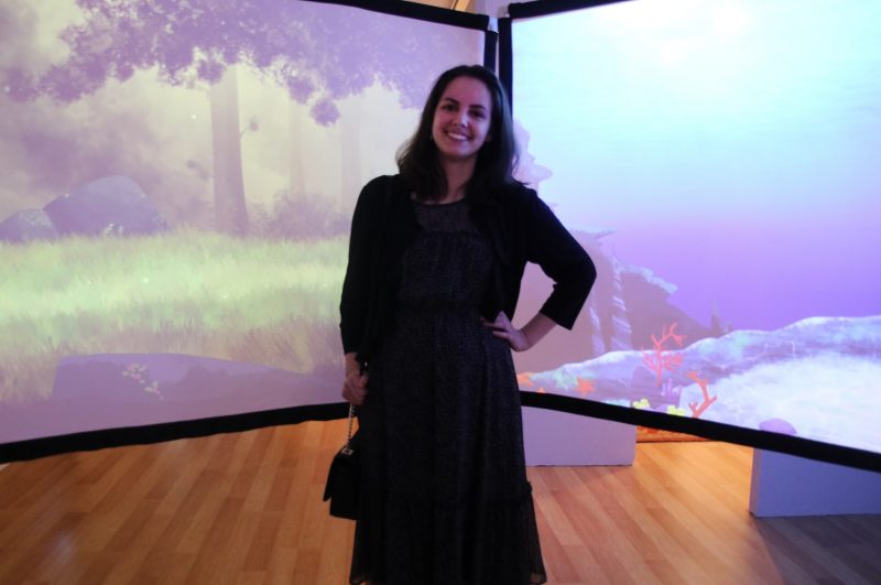 Tara Dietz standing in front of two screens with her artwork displayed.