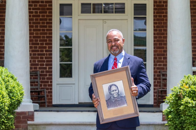 A man holds a portrait in front of a house.