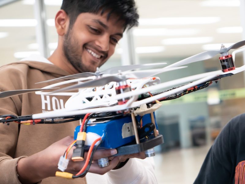 Shlok Agarwal ‘22, electrical and computer engineering, smiles as he looks at an autonomous drone that his team built to perform indoor package delivery. Photo by Chase Parker for Virginia Tech.