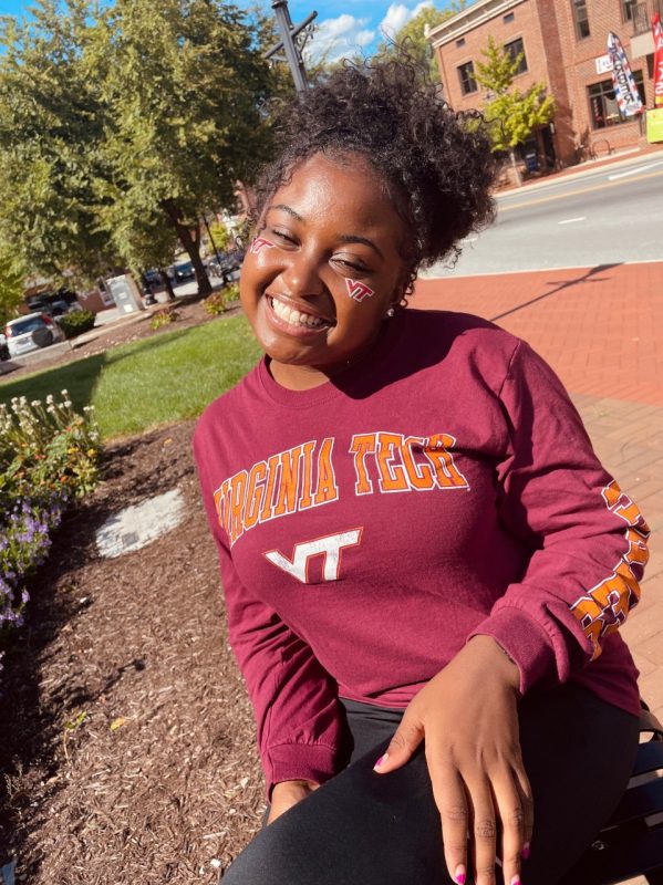 Cassidy Powers poses in downtown Blacksburg wearing a Virginia Tech t-shirt with VT stickers on her cheeks