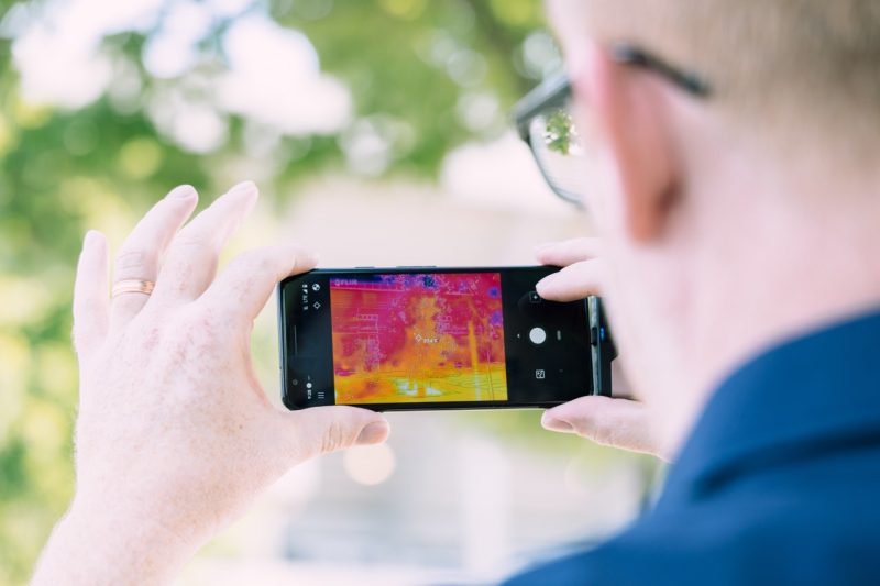 Faculty member Thomas Pingel looks at an infrared image on his smartphone that casts a parking lot in bright yellows, oranges, and fuchsias that represent heat signatures.