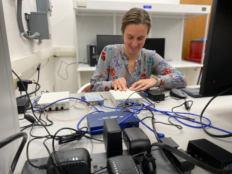 Researcher plugs a small box into a computer. 