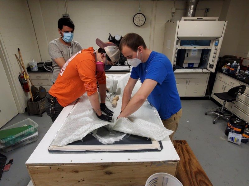 Mark Shepheard (right), along with postdoctoral researcher M. Javad Javaherian (left) and recent graduate Nicholas Scianna, works on applying the first layer of fiberglass to the team’s generic prismatic planing hull model. The construction was completed as part of Shepheard’s master’s thesis on machine learning and parametric study of slamming events