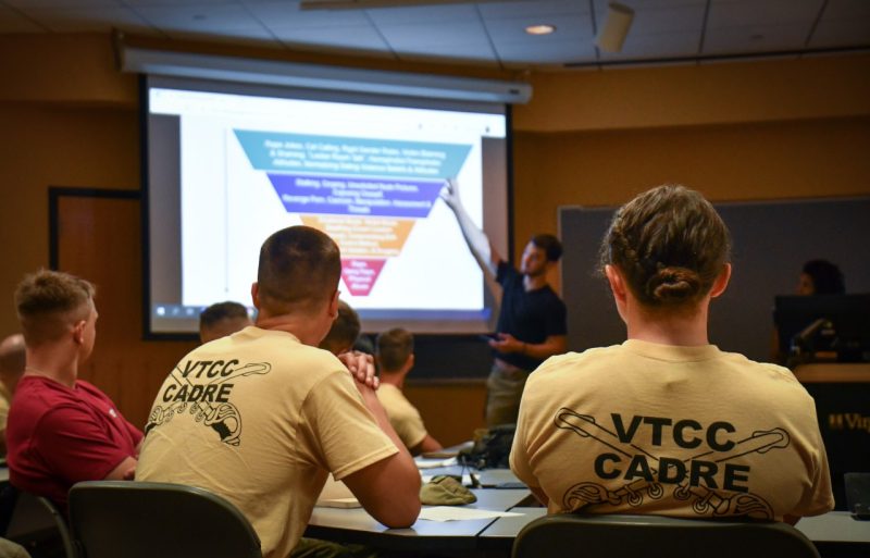 Two cadets in yellow VTCC Cadre shirts face a presentation screen and presenter while learning about sexual violence prevention. Other cadets observe training in the background.