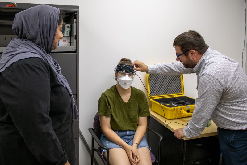 Marrium Mansoor (left) observes Ben Katz (right) demonstrate how to use the fNIRS brain-imaging machine, which Diana Devine, (center) is wearing on her head