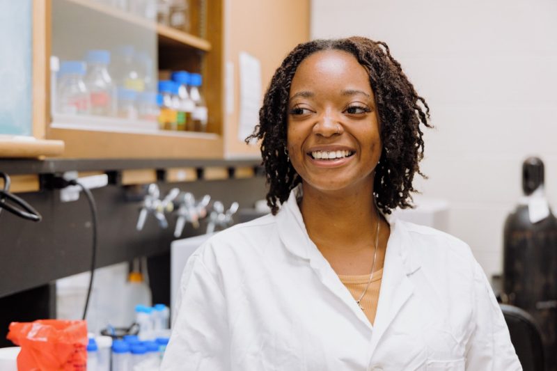 Tamesha Young, a Black woman in a lab coat, smiles as she works in an animal science lab.