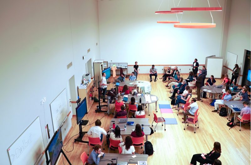 A bird's-eye view of the Honors Studio in Squires with students at tables around the room and visitors to Honors SuperStudio watching their presentations