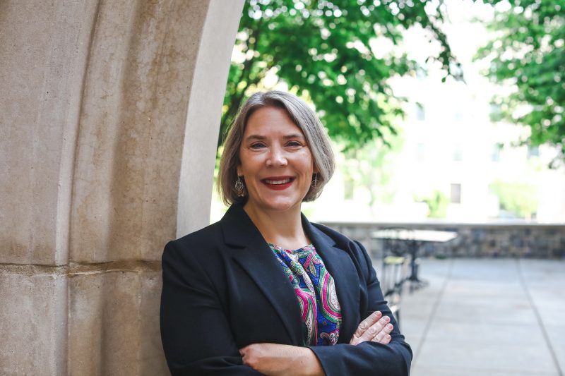 Rebecca Caldwell, Virginia Tech’s first director of Residential Well-being, stands on campus under a vaulted arch with arms crossed. 