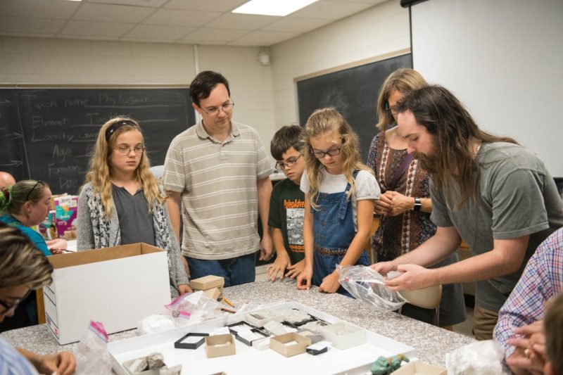 A bearded man shows youth and adults how to unwrap fossils in this 2018 file photo. 