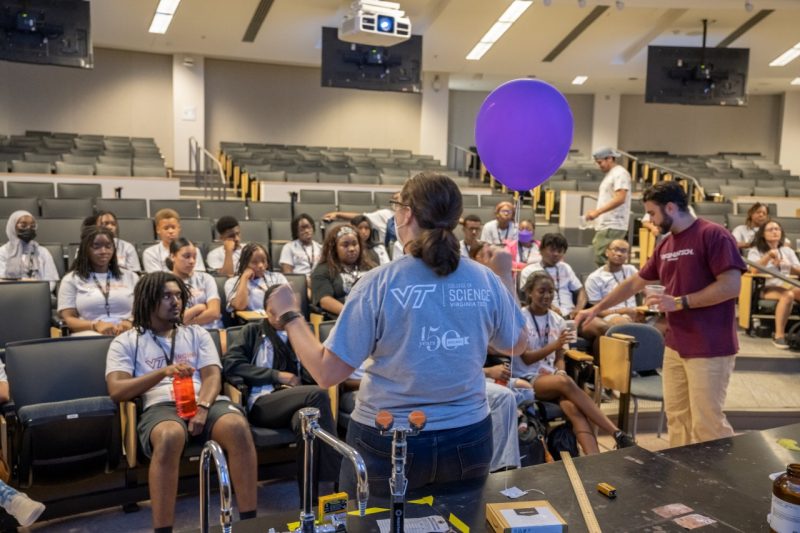 A woman, holding a balloon, gives a polymer chemistry to a group of students attending the Virginia Tech Black Collegiate Institute earlier this summer.  