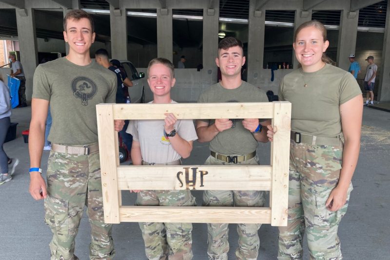 Four cadets hold up a piece of a wooden bed frame.
