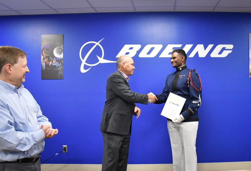  David Calhoun, president and chief executive officer of The Boeing Company, leans in to shake the hand of Cadet Vivek Gopalam. Both are standing against a blue backdrop that says Boeing in large white letters. Both are smiling.