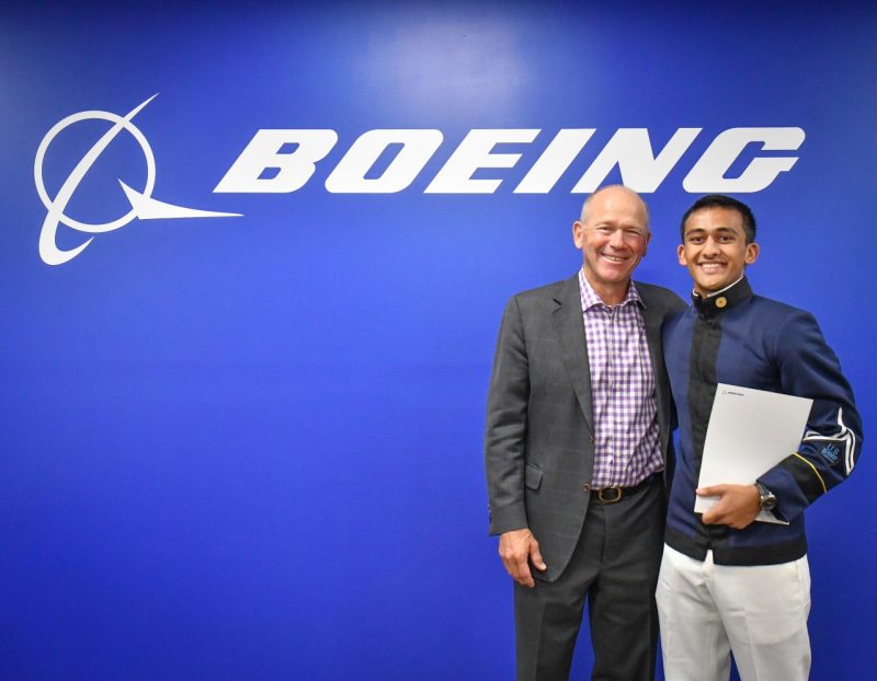 David Calhoun, president and chief executive officer of The Boeing Company, stands with Cadet Pramil Patel against a blue backdrop that says Boeing in large white letters. Calhoun has his arm around Patel and both are smiling.