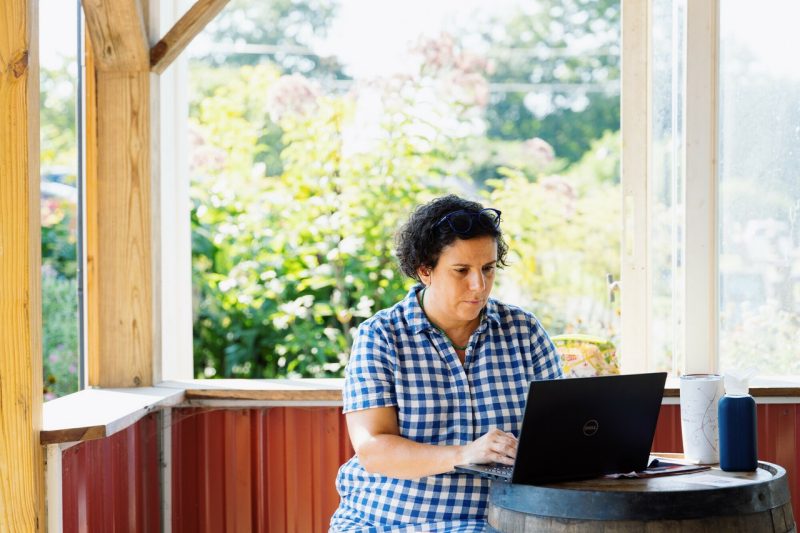 Catherine Piche, a woman in a gingham shirt, types on her laptop framed by a window during a writing retreat sponsored by the Office of Faculty Affairs.