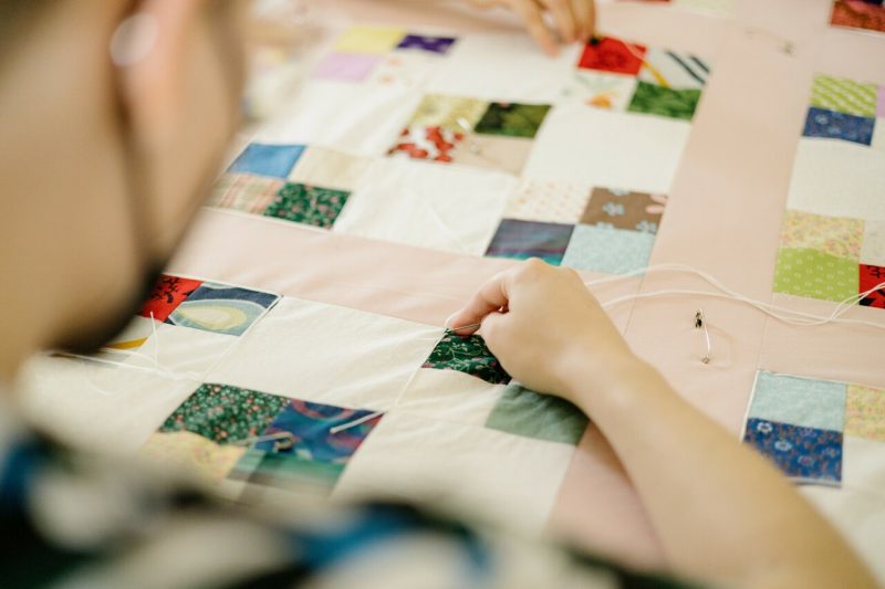 A student works a needle through a patchwork quilt top as part of a quilt-tying event.
