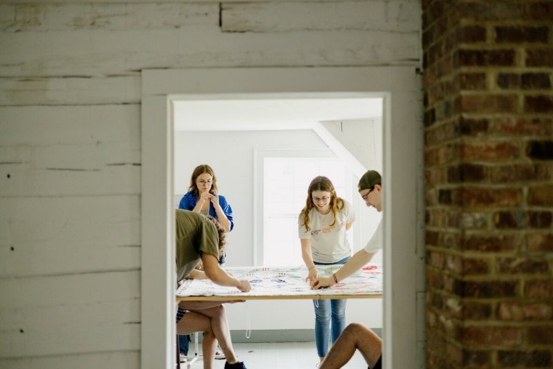 Students are seen through a doorway in the historic Fraction House as they tie a patchwork quilt.