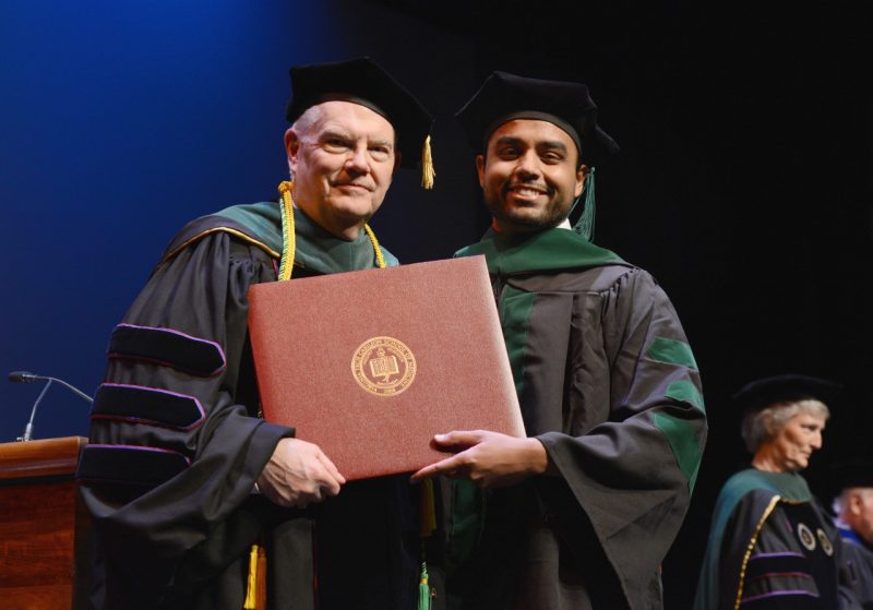 Interim dean Dan Harrington holds a diploma along with student Sahal Thahir at the Virginia Tech Carilion School of Medicine's 2019 graduation. 