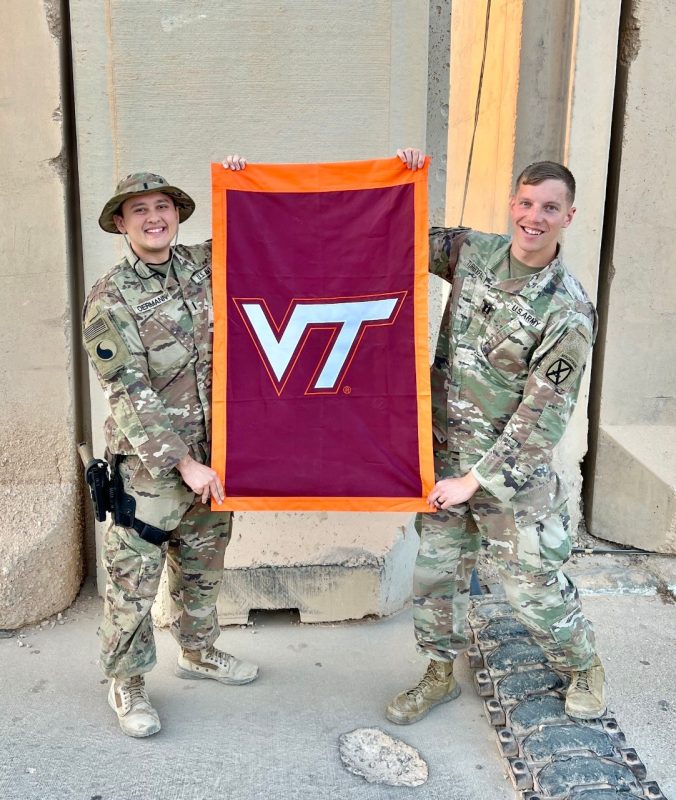 First Lieutenant Oermann and Captain James Turbyfill stand in camouflage uniforms holding a Virginia Tech flag. Both are smiling. 