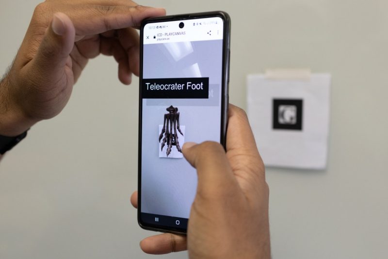 A hand is holding a cell phone on which a dinosaur foot is displayed.