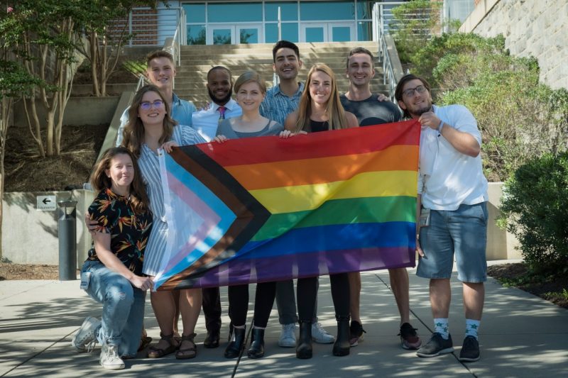 Nine individuals holding a pride flag.