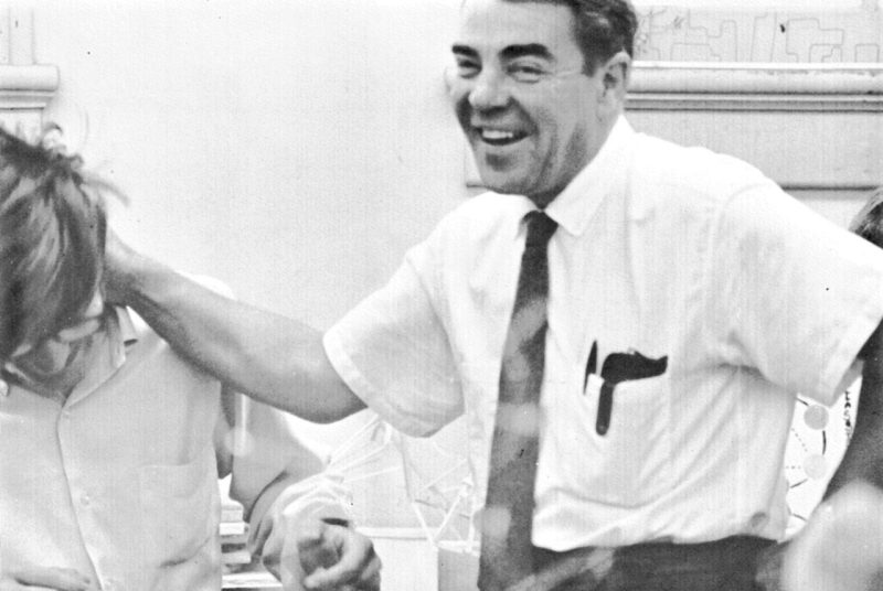 Dean Carter, wearing a white shirt and tie, laughs as he puts his hand on a student's shoulder.