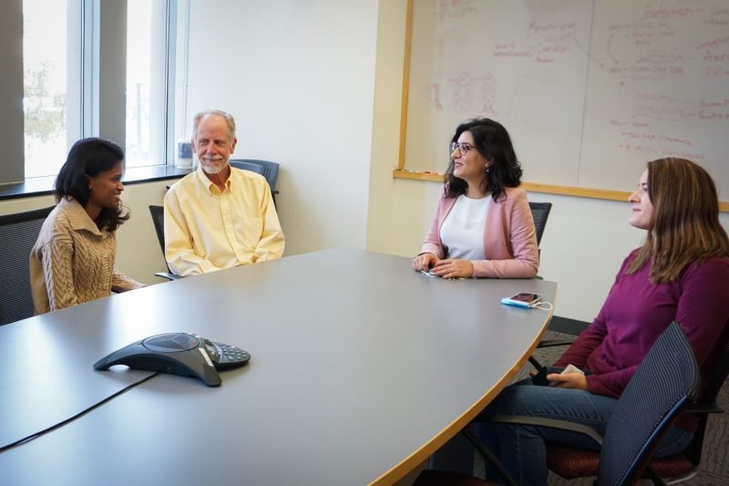 Four people sit around a conference table smiling and having a conversation.