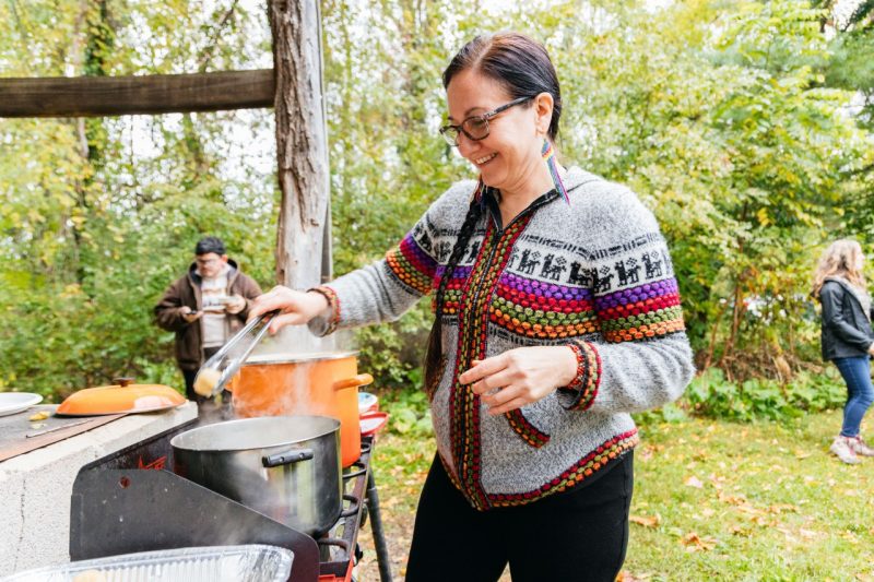 In a brightly colored sweater, Peruvian guest chef Krysia Villón cooks soup on a camping stove in the outdoor kitchen.