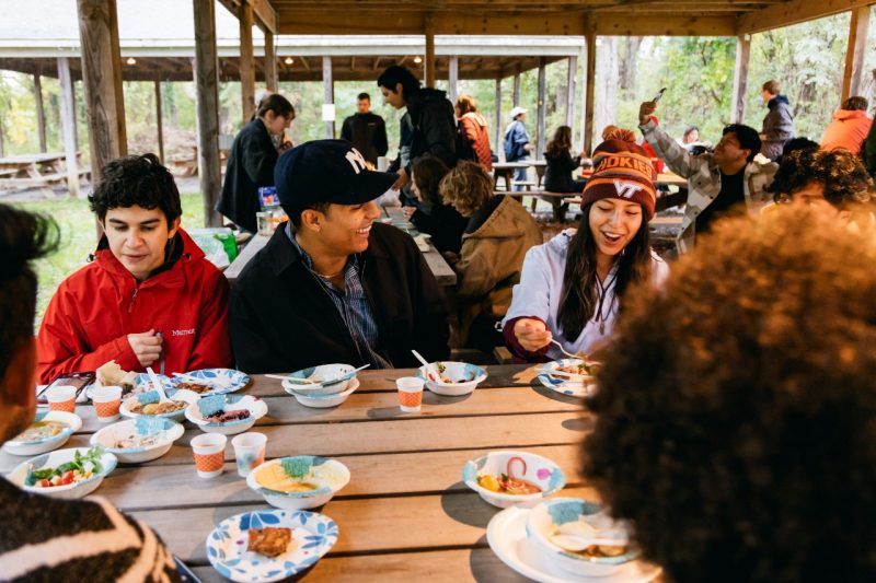 Students laugh and eat around a picnic table at the Indigenous Friendship Garden cooking demonstration.