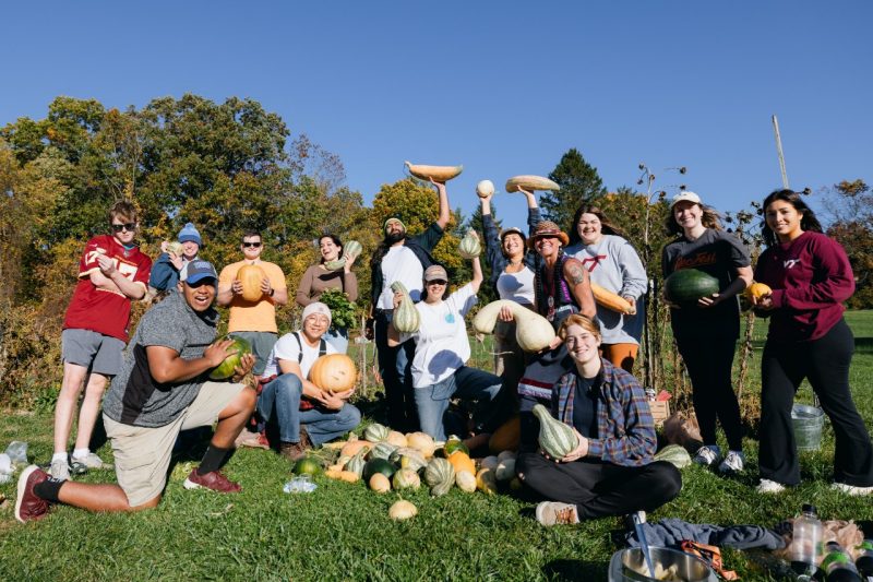 Under a blue sky, a group of students and faculty members proudly display different kinds of squash they harvested from the Indigenous Friendship Garden, at Virginia Tech's Turfgrass Research Facility.