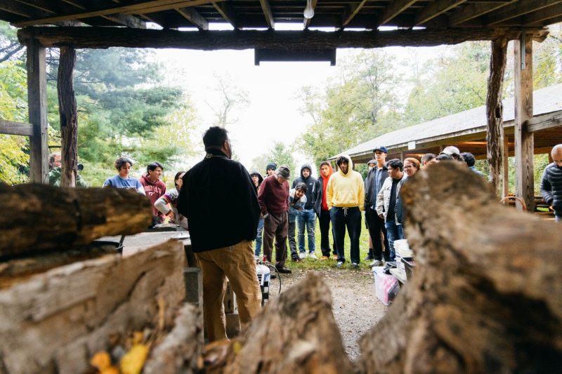 In front of a stack of wood, Mohawk chef Dave Smoke-McCluskey demonstrates corn nixtamalization to an attentive group of students.