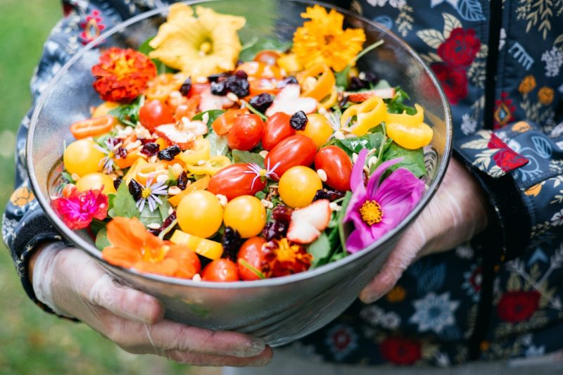 A gorgeous, brightly colored bowl of salad, the greens topped with red and yellow tomatoes, peppers, and edible flowers. 