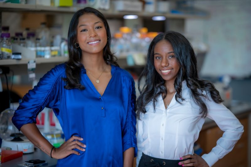 Undergraduate students Sydnee Harrison and Deborah Thomas pose together in a biomedical lab.