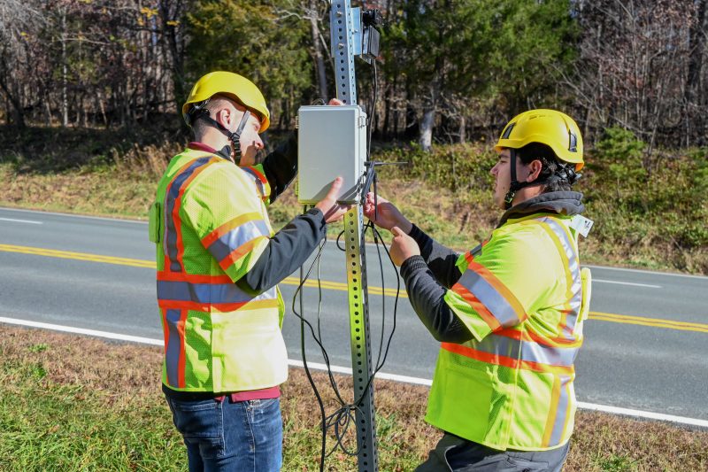 VTTI researchers dressed in roadside safety gear installing part of the VTTI Smart Work Zone on a road sign.