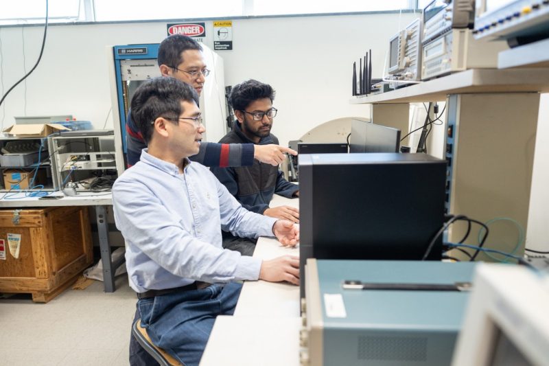 students and professor discuss research findings they are looking at on a computer screen in a lab.